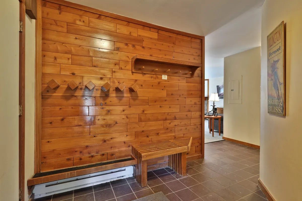 This image features a cozy entryway with wooden wall paneling, a bench for sitting, coat hooks, and a shelf. The design evokes the first welcoming moments of arriving back from outdoor adventures, and the space is clearly set up for guests to take off winter gear like boots and coats.