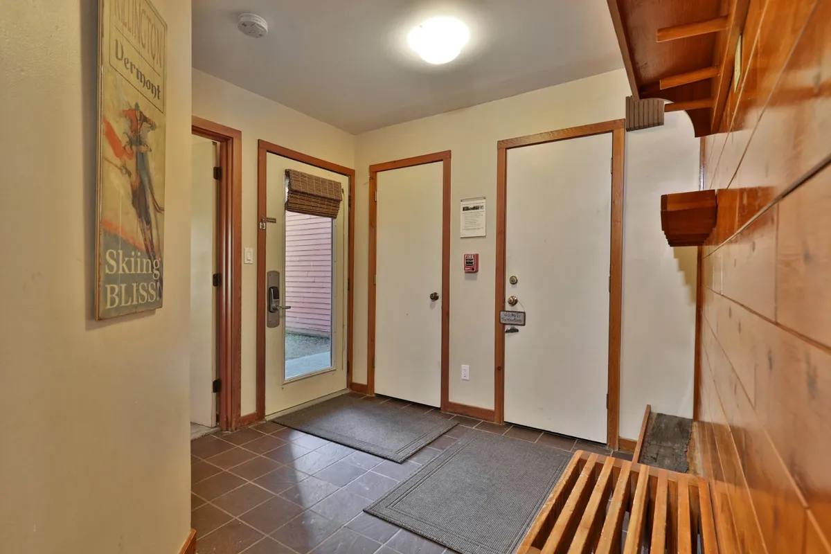 A welcoming entryway featuring a wooden bench, a cozy mat, an entrance door, and a vintage skiing poster on the wall. The setting feels functional yet inviting—ideal for greeting guests as they come and go for nights out or après-ski adventures.