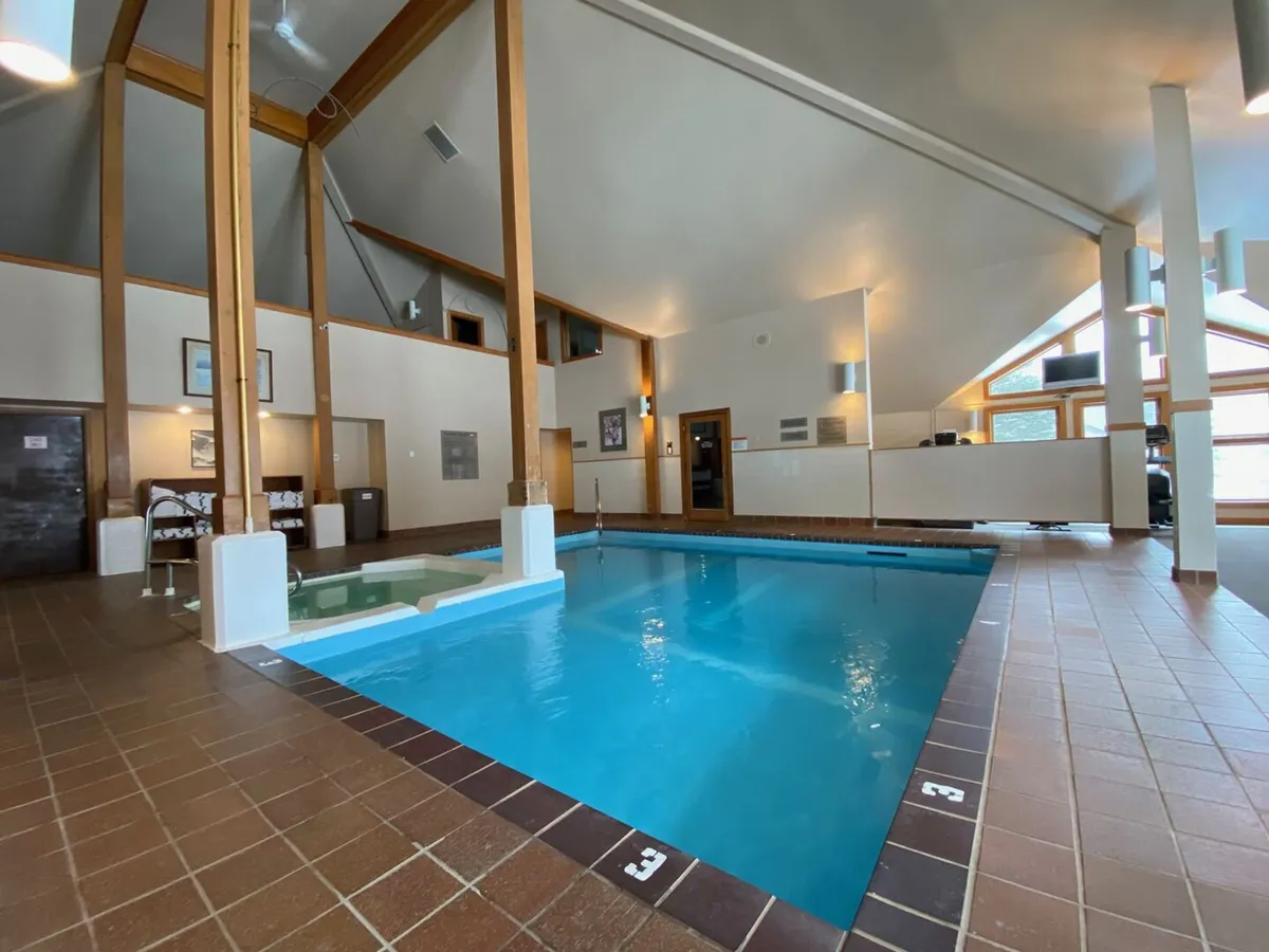 This image showcases the indoor saltwater pool, featuring large windows that allow natural light to flood the area and wooden beams that create a warm, inviting ambiance. The reception area hints at guest services and facility access.