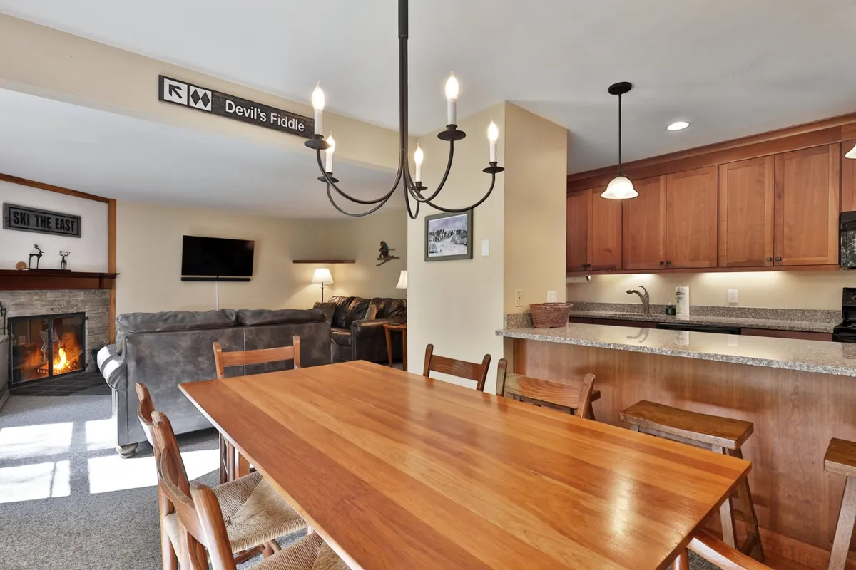 A spacious, open-concept interior featuring a dining table, chandelier, fireplace, living area, and kitchen counter—all visible in one inviting shot. The area is set up for group meals, celebrations, or game nights, perfectly aligning with the section’s mention of a cozy night in.