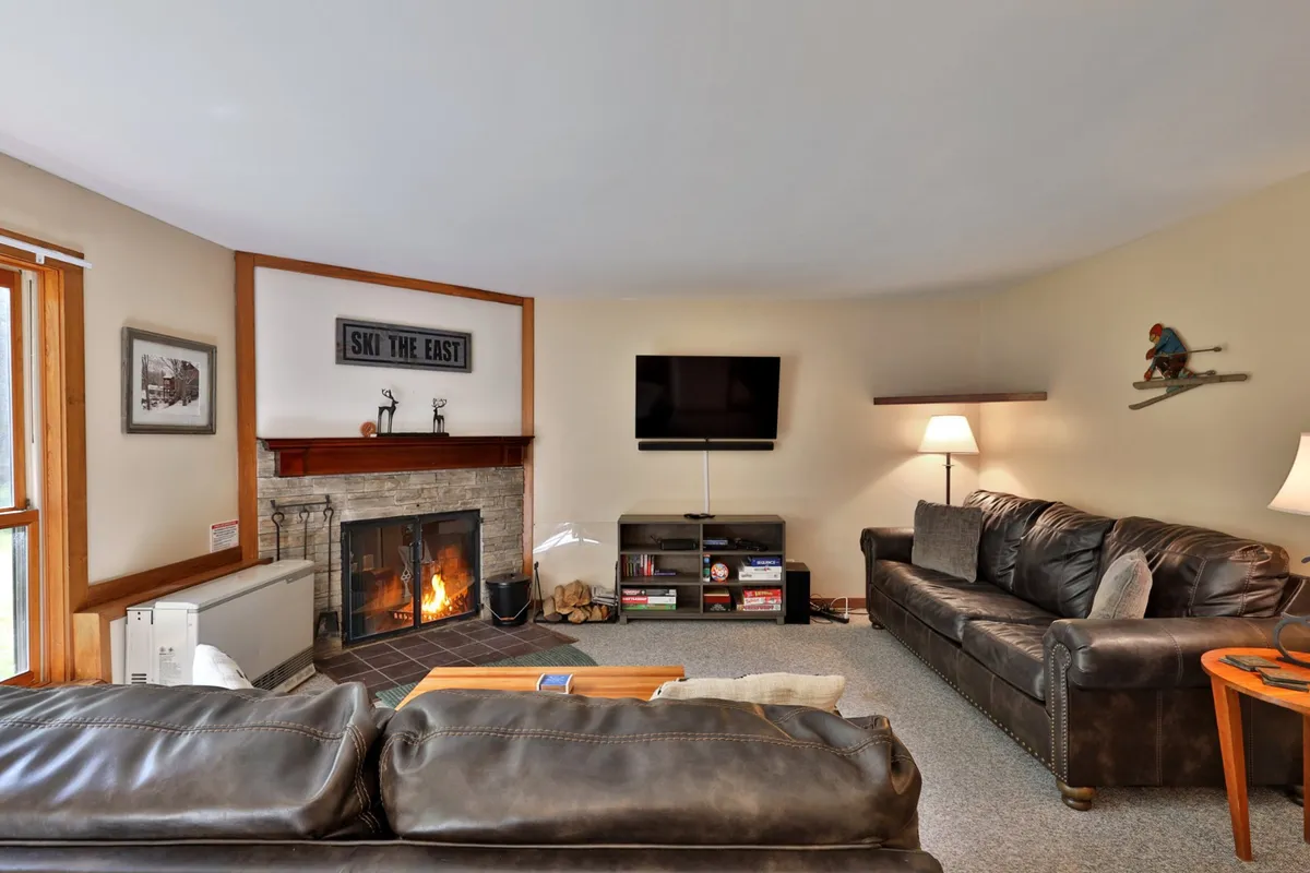 This image showcases a warmly lit living room featuring a central fireplace flanked by plush sofas and a television. The space radiates comfort and invites visitors to gather, unwind, and enjoy entertainment together. The harmonious arrangement ensures there is ample seating for group relaxation.