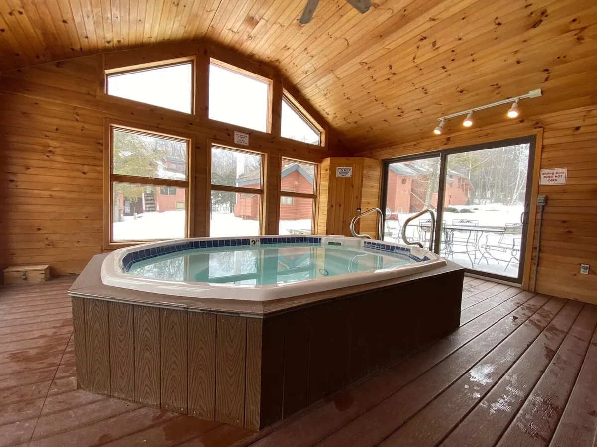 This cozy interior shot features the hot tub surrounded by large windows and wooden beams, creating a relaxing environment for unwinding after outdoor adventures.
