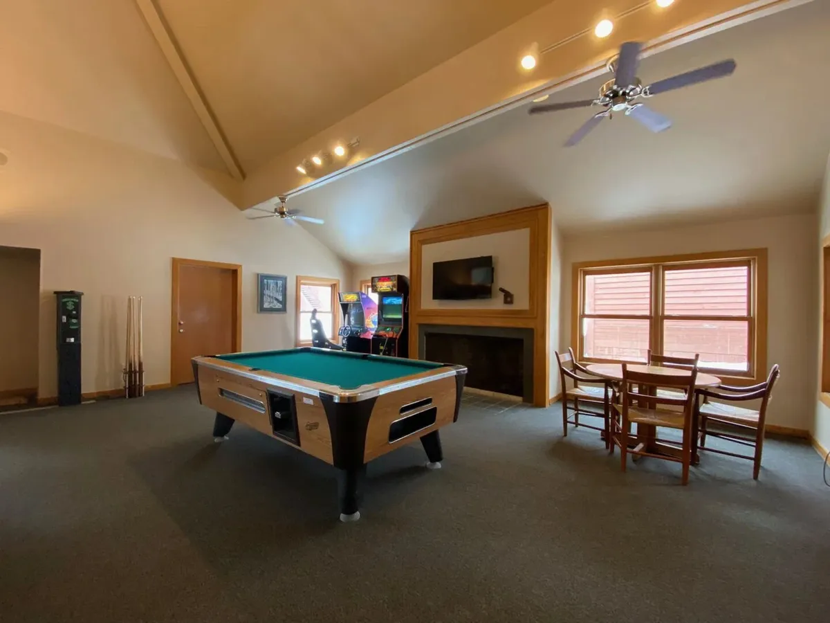 A lively interior scene depicting the game room, complete with a pool table, arcade machine, dining table, and fireplace, capturing both recreational fun and social gatherings.